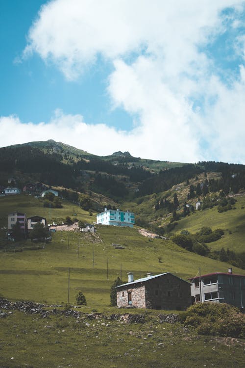 Peaceful scenery of remote village with cozy small cottages located on grassy hills during clear sunny day