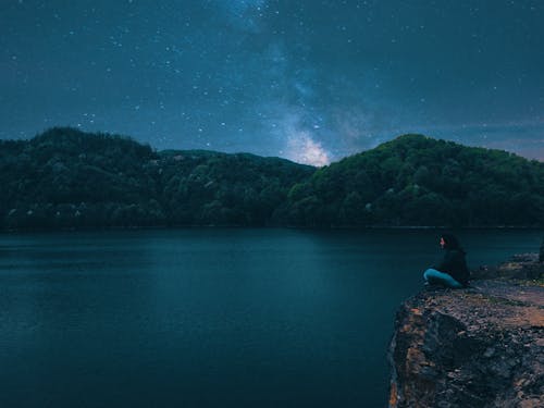 Woman Sitting on Peak Front of Calm Water at Night