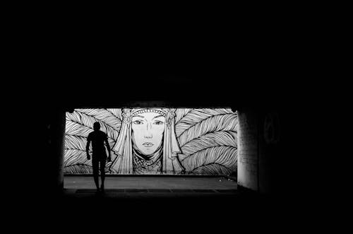 A man is standing in the dark under a tunnel with a mural