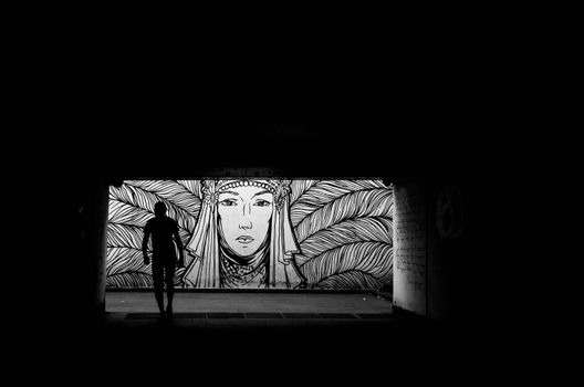 Black and white tunnel photo in Tbilisi featuring a silhouette against mural art.