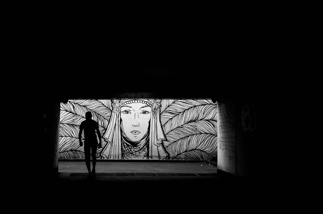 A man is standing in the dark under a tunnel with a mural