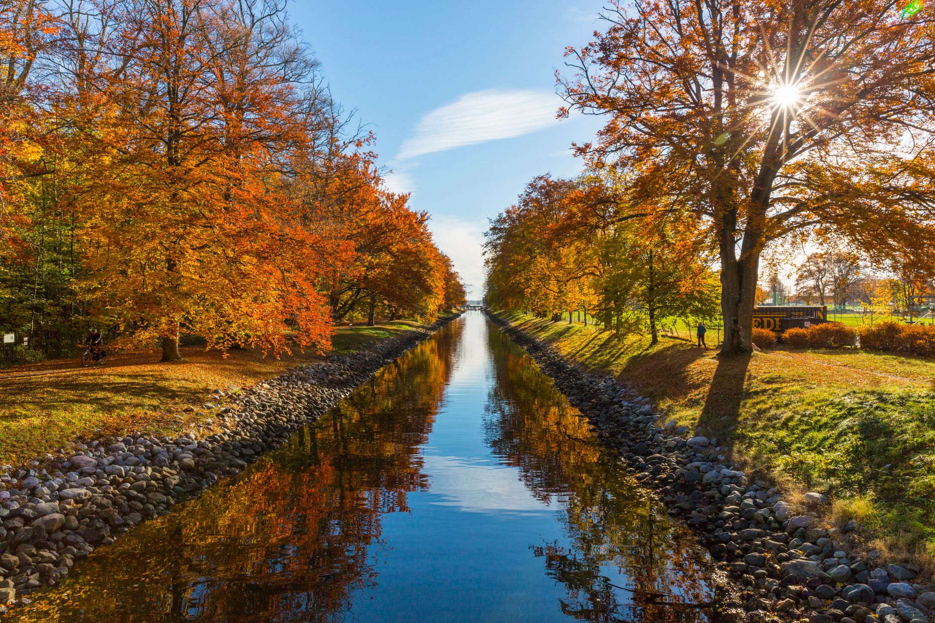 A picturesque canal scene in Horten, Norway, showcasing vibrant autumn foliage and clear blue skies.