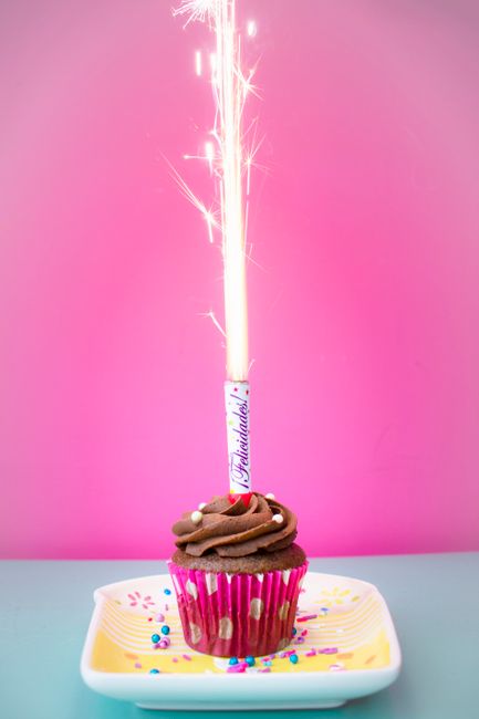 Colorful chocolate cupcake with a sparkling candle against a vibrant pink background.