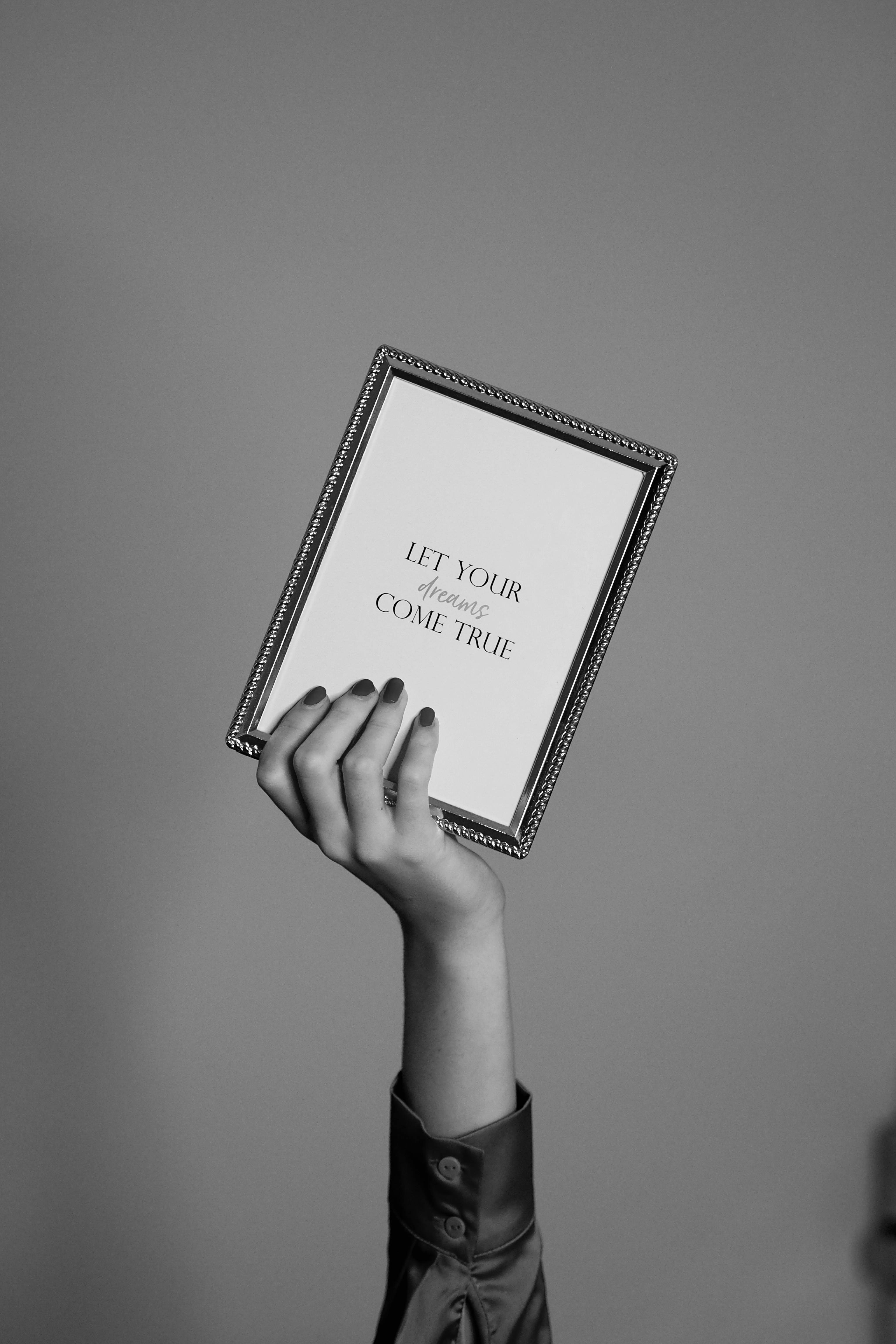 Black and white image of a hand holding a framed inspirational quote.