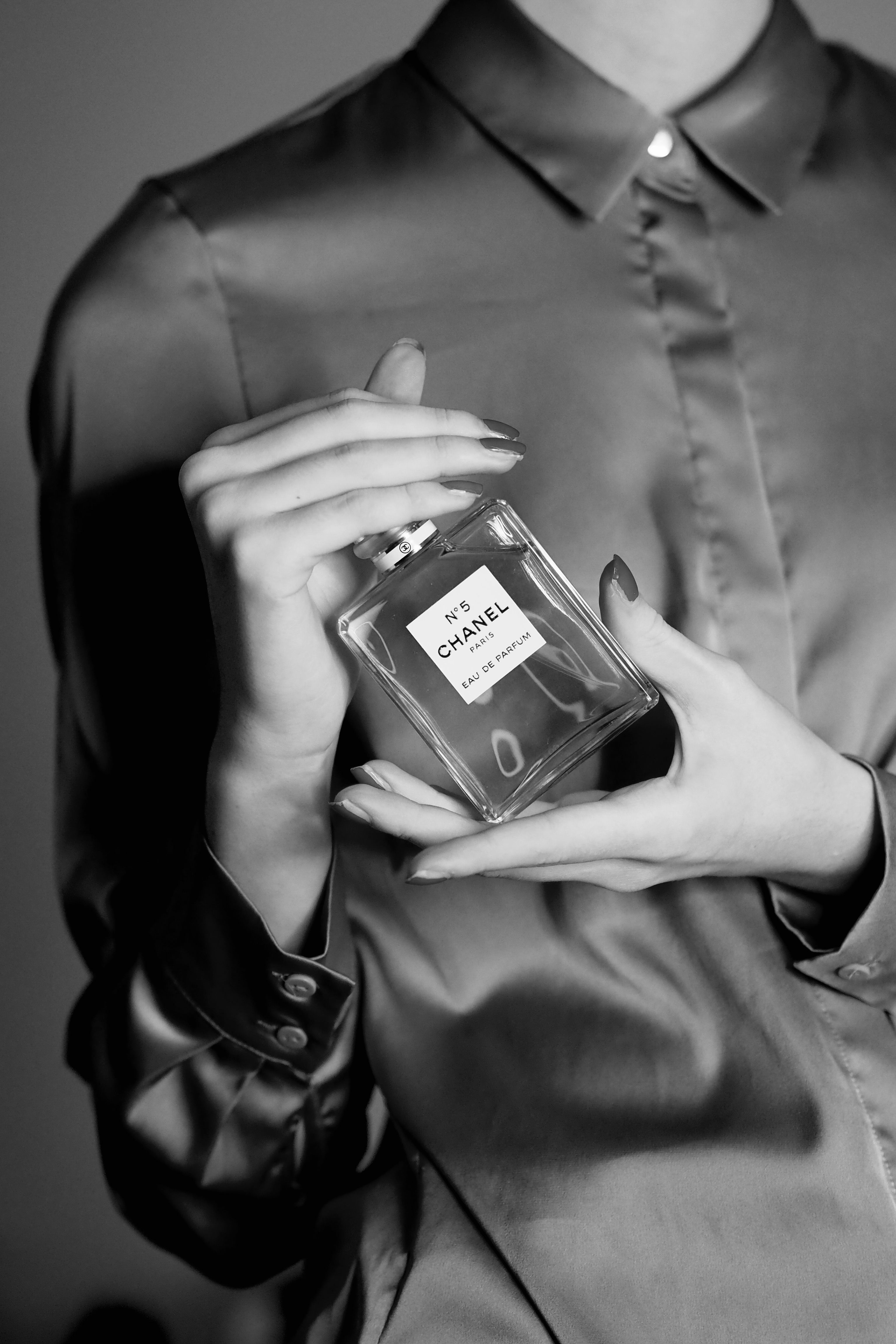 Black and white image of a woman holding a Chanel perfume bottle in a satin blouse.