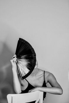 Black and white portrait of a woman elegantly posing with a fan in a Paris studio.