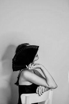 Artistic black and white portrait of a woman seated with a hand fan.