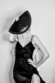 Stylish black and white portrait of a woman posing with a hand fan in a Parisian studio.