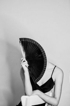 Black and white studio portrait of a woman with a hand fan, exuding elegance.