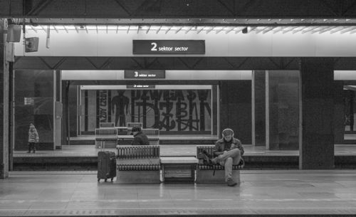 Free A serene black and white photo of people waiting at an urban train station with benches and signs. Stock Photo