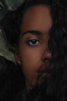 Artistic close-up portrait of a woman with long hair partially covering her face, surrounded by natural leaves.