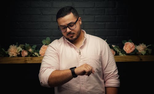 A man in a pink shirt looking at his watch