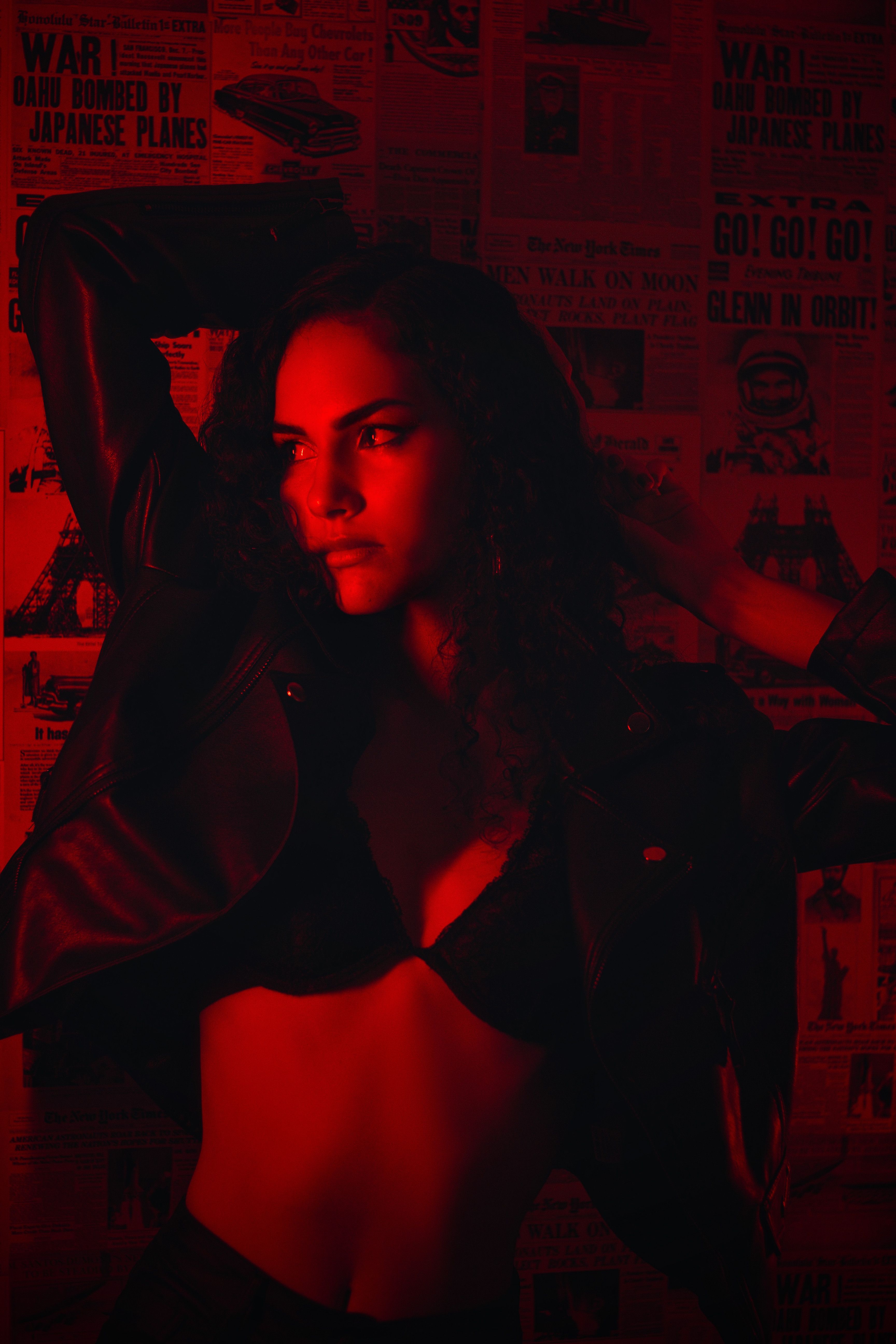 A captivating portrait of a young woman in a black bra and leather jacket, illuminated by moody red lighting.
