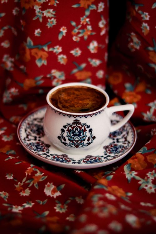 Free Elegant coffee cup on ornate saucer set against a vibrant red floral fabric backdrop. Stock Photo