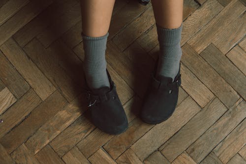 A person wearing black shoes and socks on a wooden floor