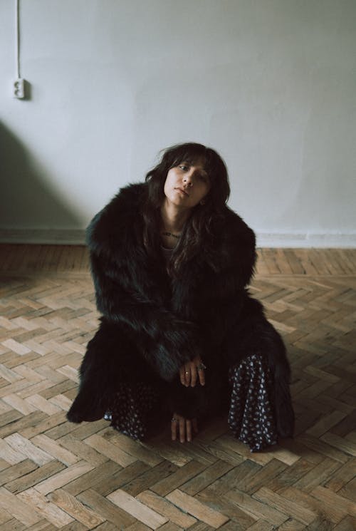 A woman in a black fur coat sitting on the floor