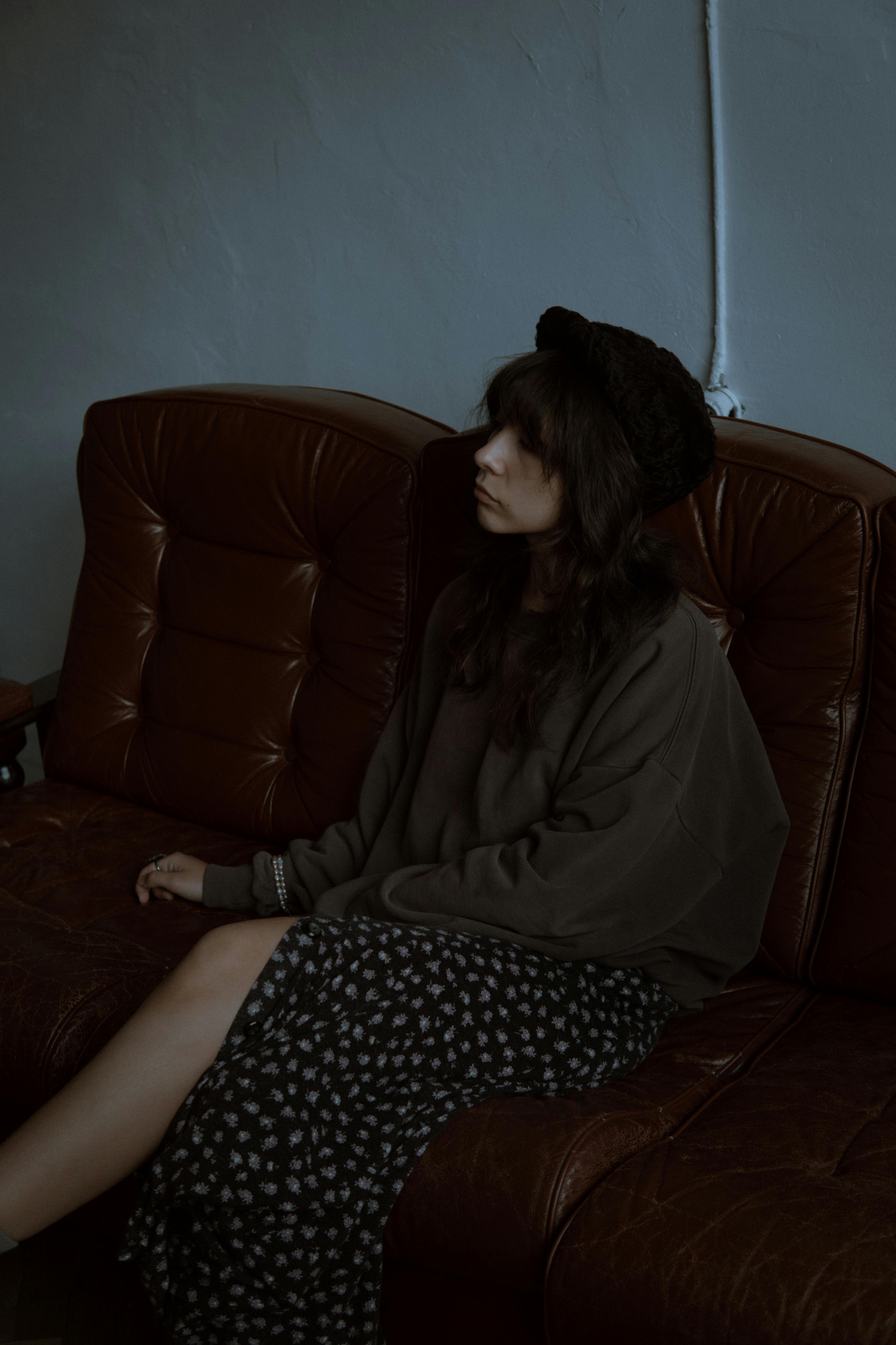 Pensive woman in beret seated on a leather couch, exuding moody ambiance.