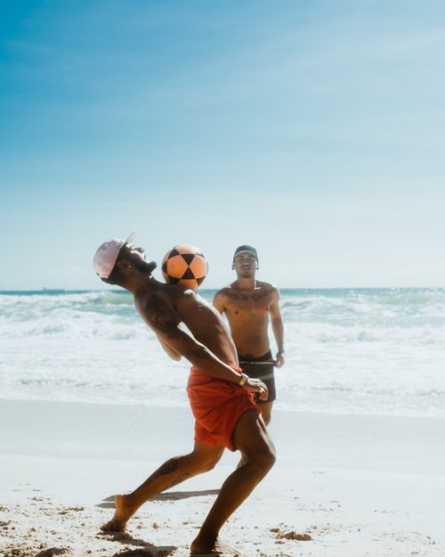 Free Two men enjoying a fun game of football on a sunny beach day. Stock Photo