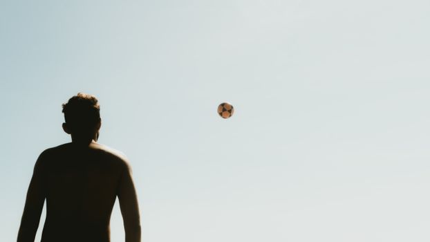 Silhouette of a man looking at a football in the sky, captured during a warm summer day.