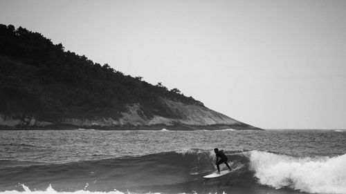 Free Monochrome image of a surfer catching waves near a rugged coastline. Stock Photo