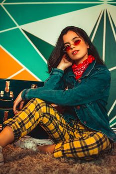 Fashionable woman posing with vibrant geometric background wearing plaid pants and denim jacket.