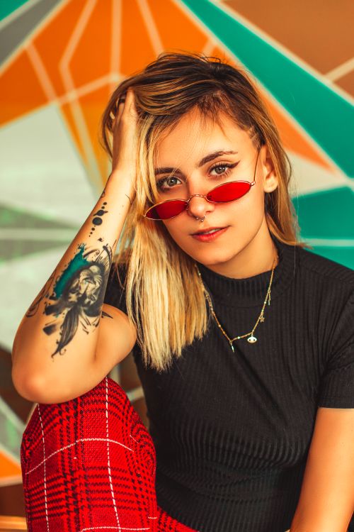 Free Fashionable woman with sunglasses and tattoo posing in front of a colorful geometric background. Stock Photo