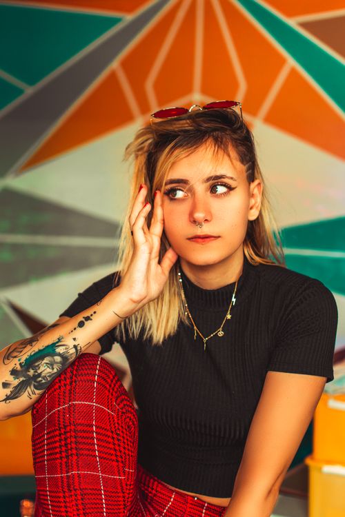 Free Stylish young woman sits thoughtfully in front of a colorful geometric mural. Stock Photo