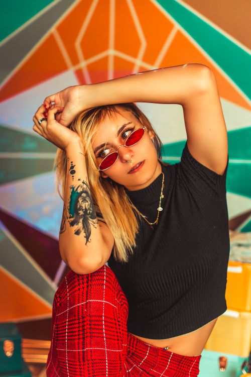 Free Trendy woman poses confidently with tattoos and sunglasses against a colorful geometric background. Stock Photo