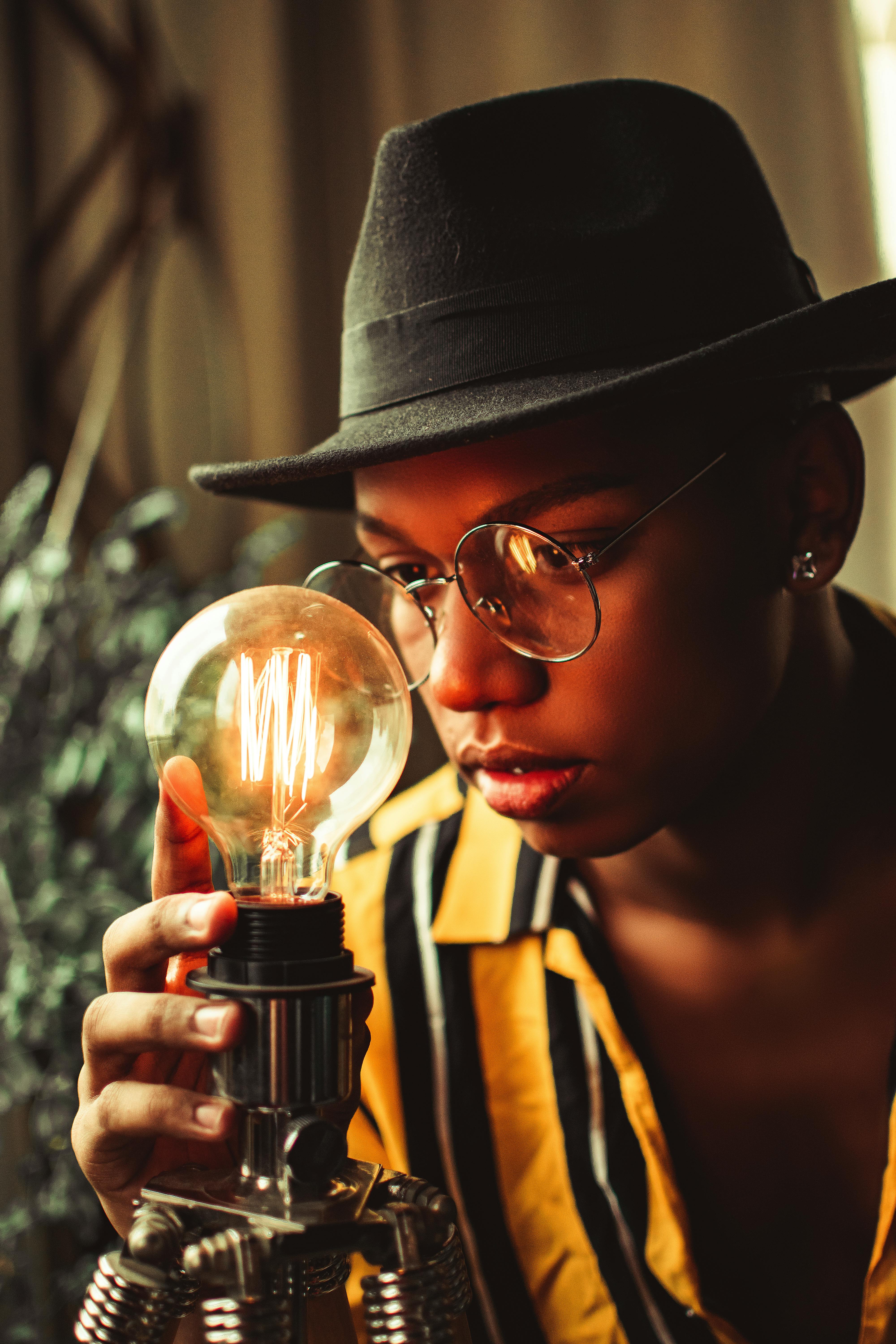 室内，一位戴着帽子的时尚年轻人正在检查发光的灯泡