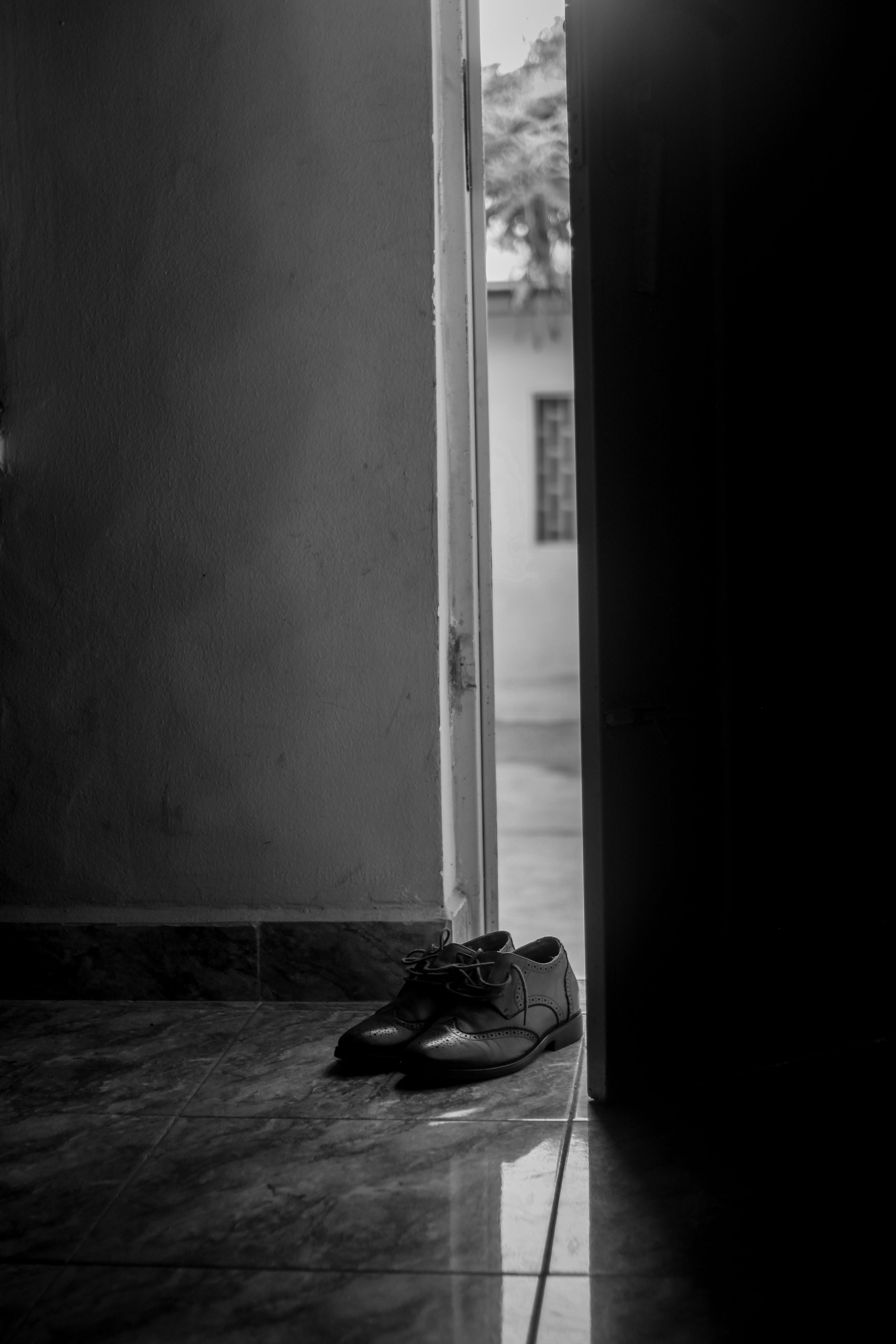 Black and white image of elegant shoes by an open doorway, creating a dramatic entrance.