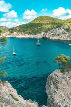 Sailboats drift in a stunning turquoise bay surrounded by rocky cliffs in Ibiza, Spain. by Kevin Kobal