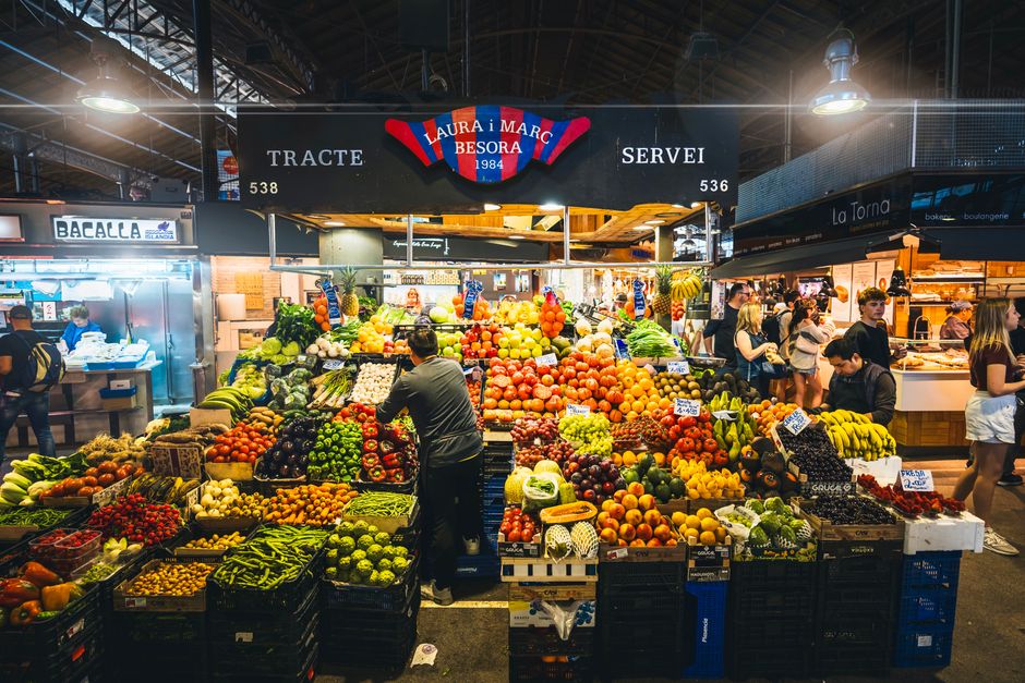 Puesto colorido que exhibe frutas y verduras frescas en el bullicioso mercado de Barcelona.