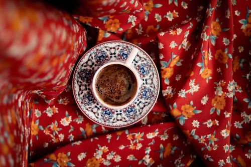 Free Top view of a coffee cup on ornate porcelain over red floral fabric, vibrant and inviting. Stock Photo