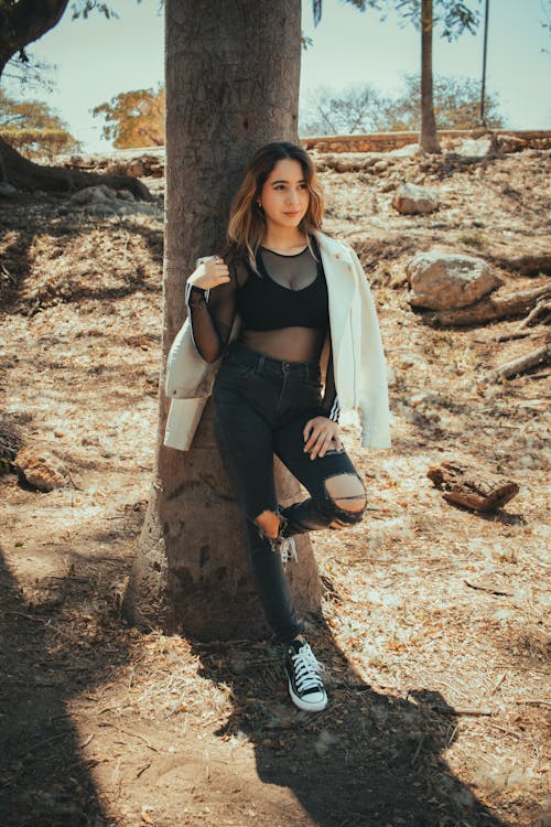 A woman in black pants and a top posing near a tree