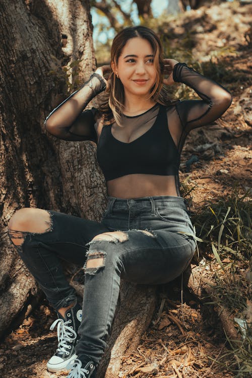 A woman in black top and ripped jeans sitting on a tree