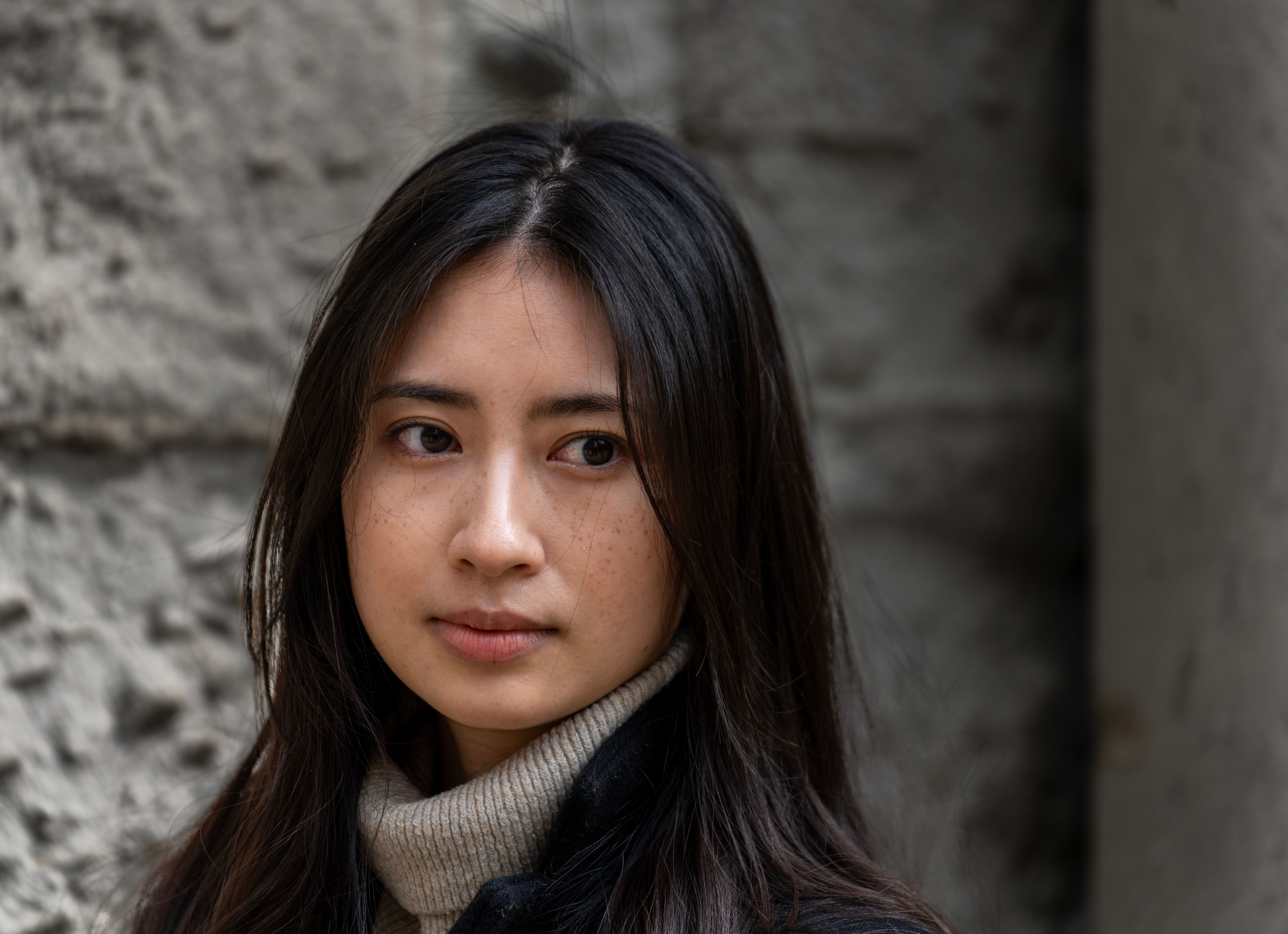 Portrait of a woman deep in thought, framed by urban stone walls providing a neutral background.
