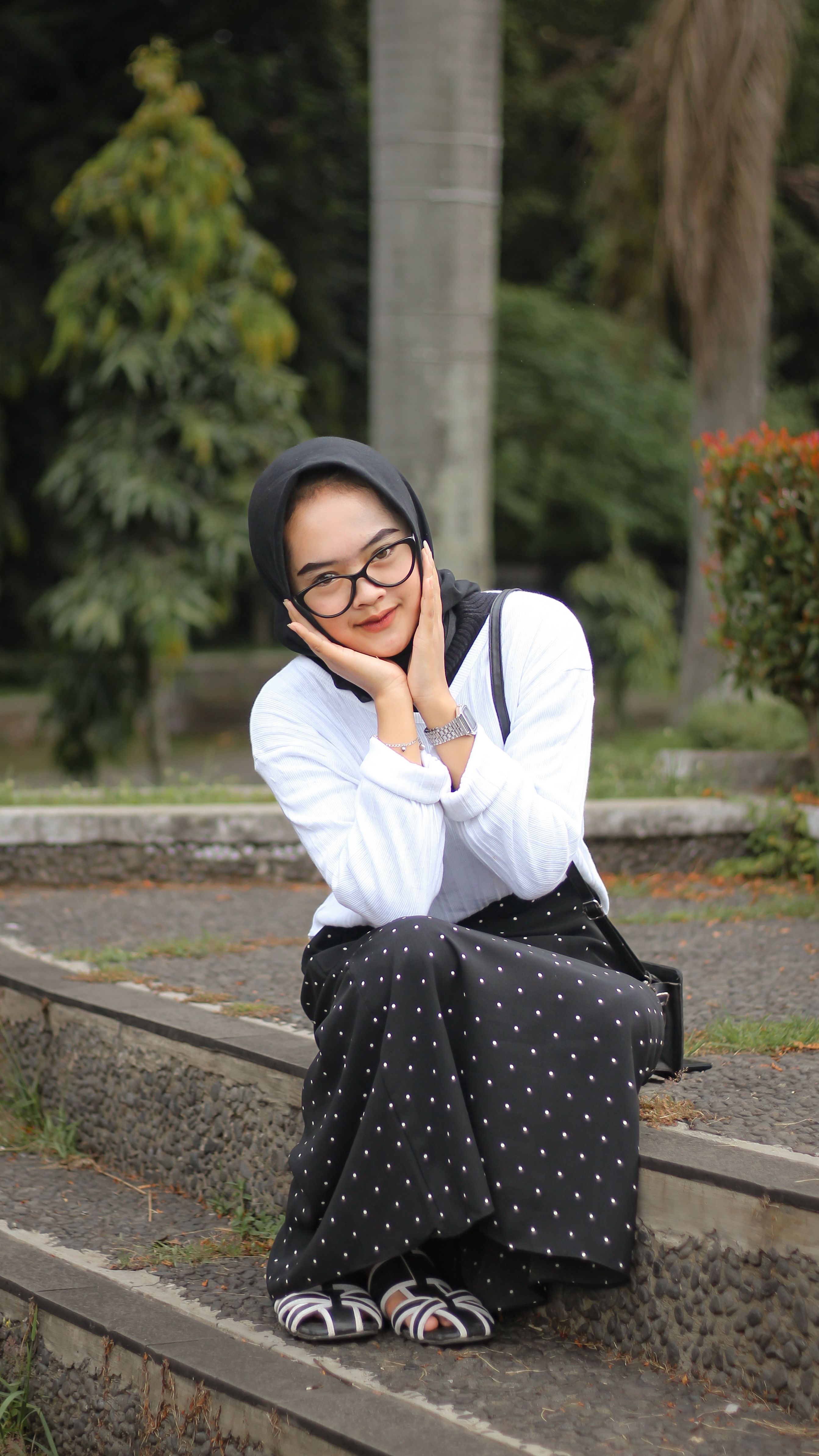Fashionable woman with headscarf and eyeglasses posing on outdoor steps in a relaxed manner.