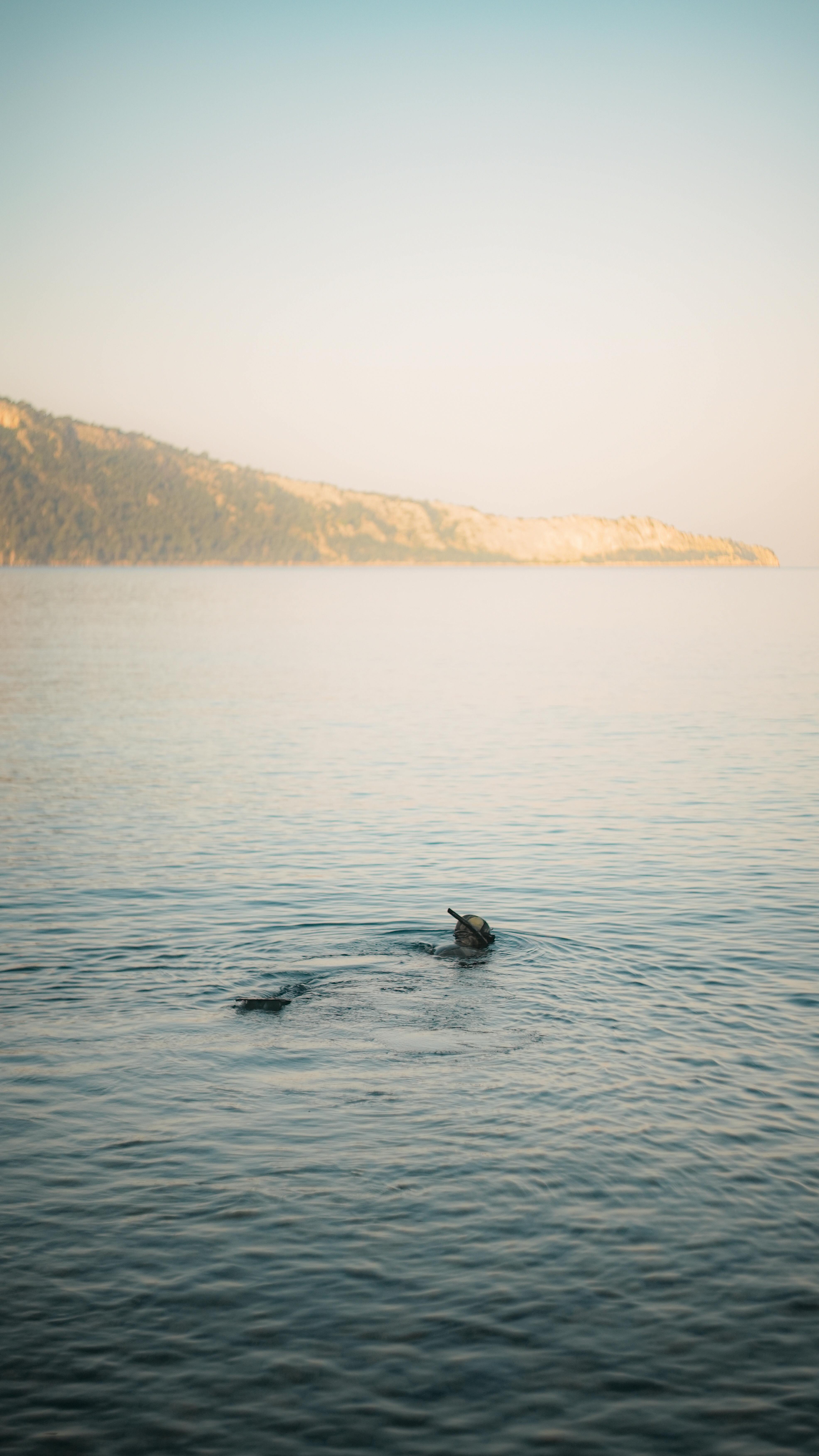 Serene image of a lone swimmer in calm ocean waters against a distant coastline, perfect for vacation themes.