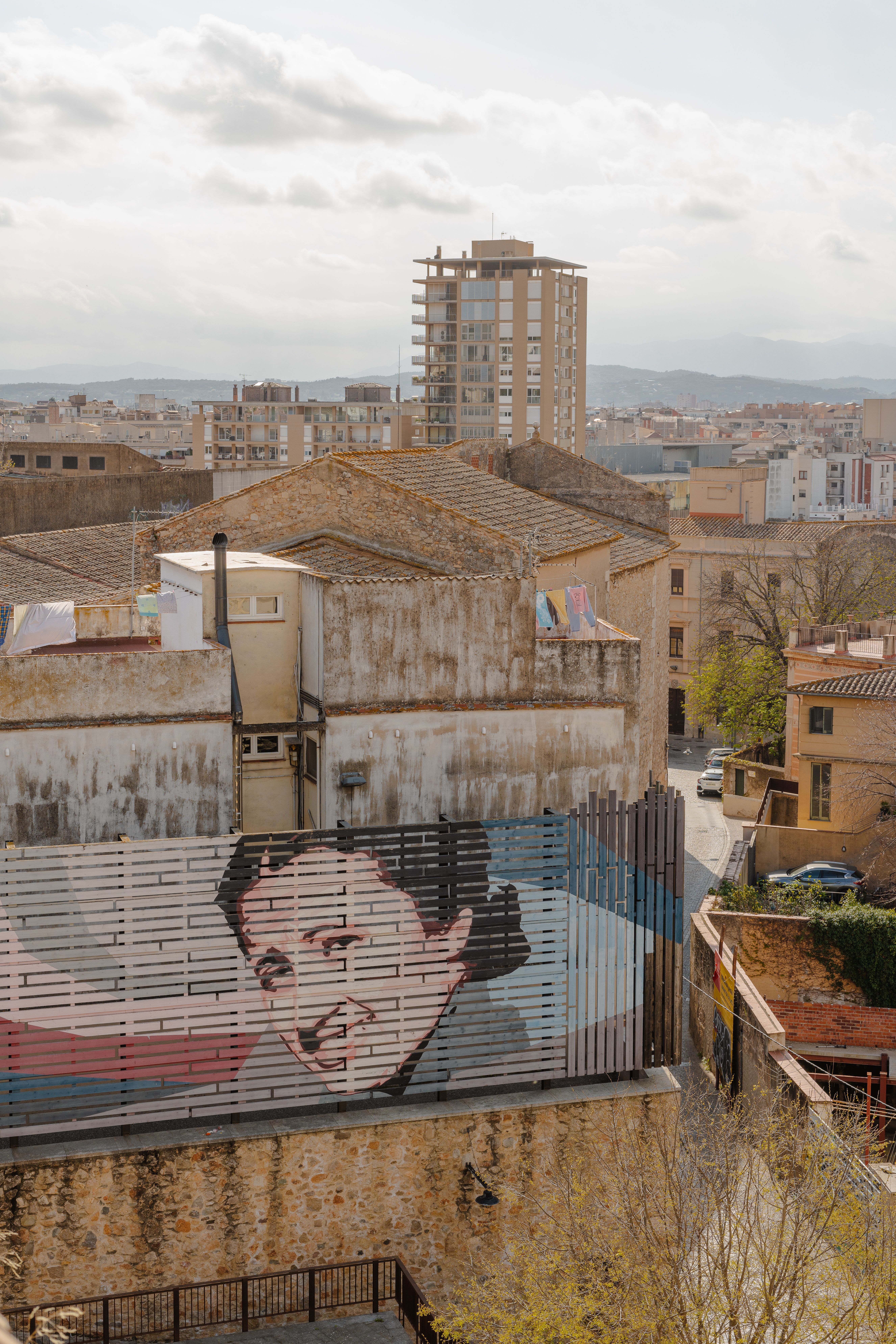 Aerial view of a mural in Girona, Spain amidst historic and modern buildings.