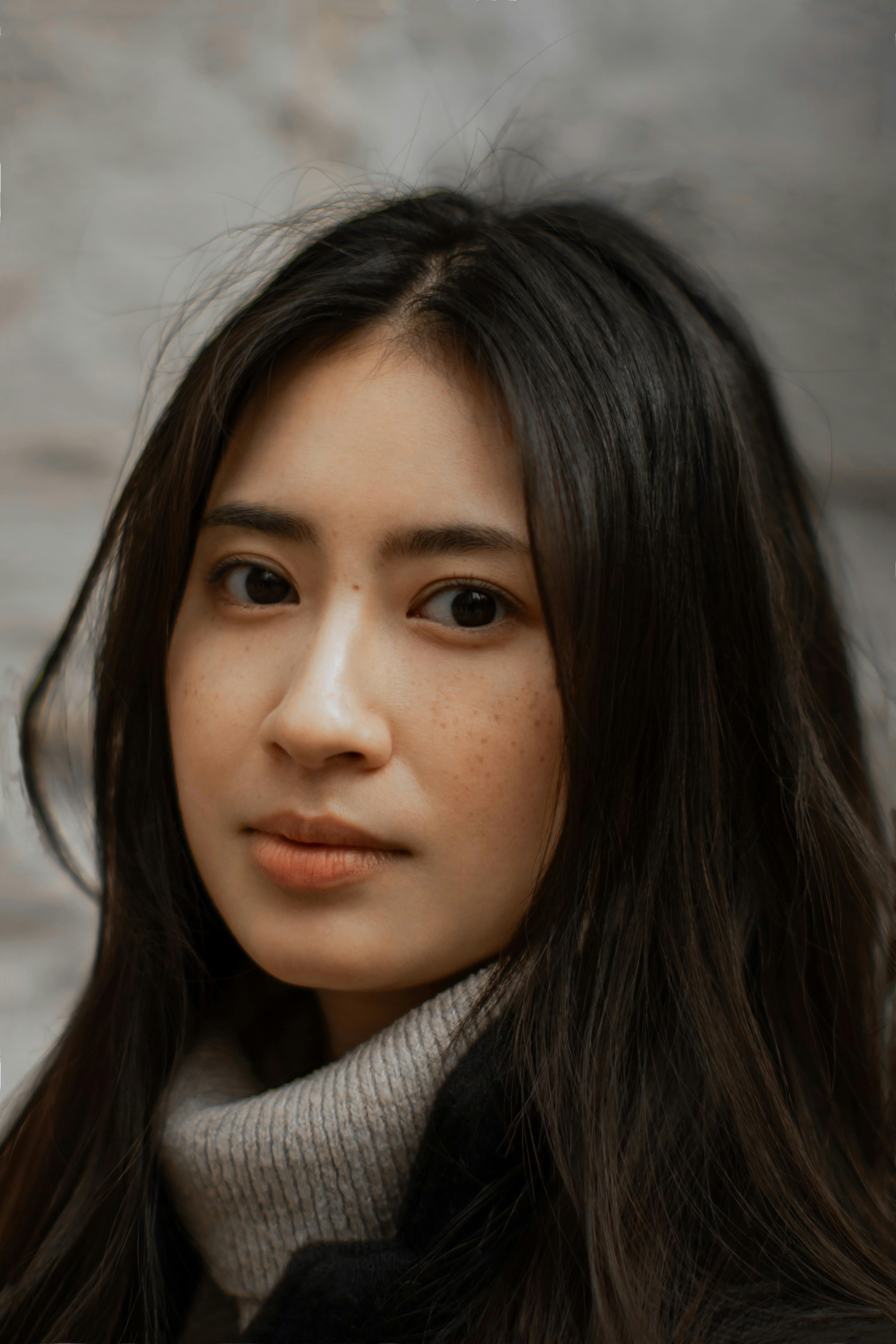 Close-up portrait of an Asian woman with long black hair, captured outdoors in a contemplative mood.