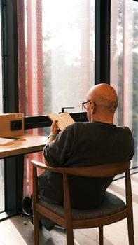 A senior man enjoys a book by the window, capturing a serene library moment.