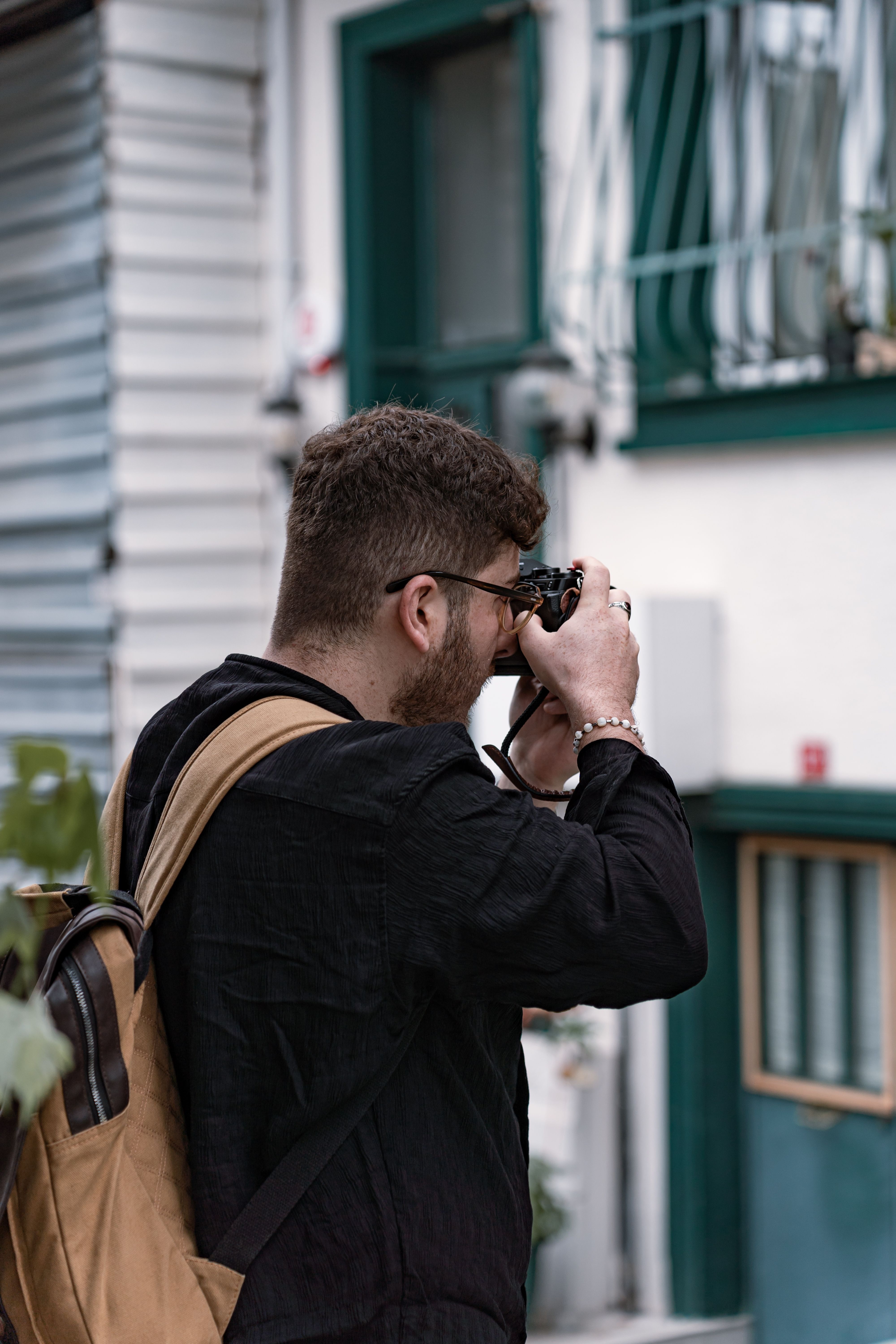 Man taking a photograph with a camera in an urban setting, carrying a backpack.