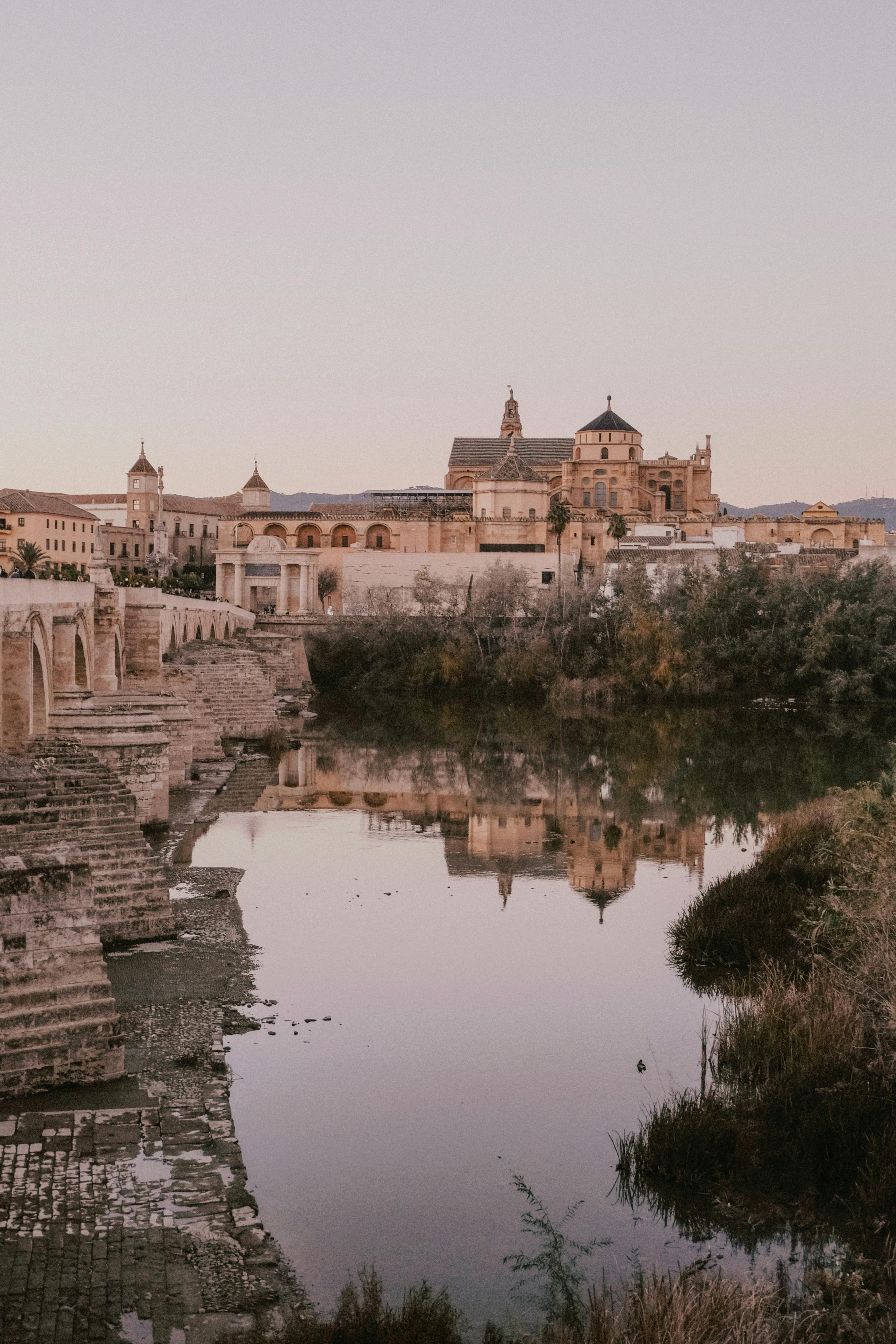 A serene landscape showcasing the Roman Bridge and historic Mosque-Cathedral of Cordoba at dusk.