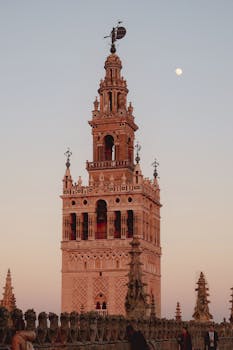 The iconic Giralda Tower in Seville, Spain, captured at dusk with a clear sky and moon.