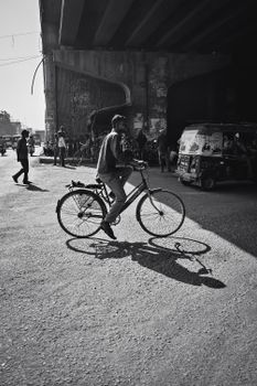 Black and white photo of a man bicycling under a city bridge, capturing urban life.