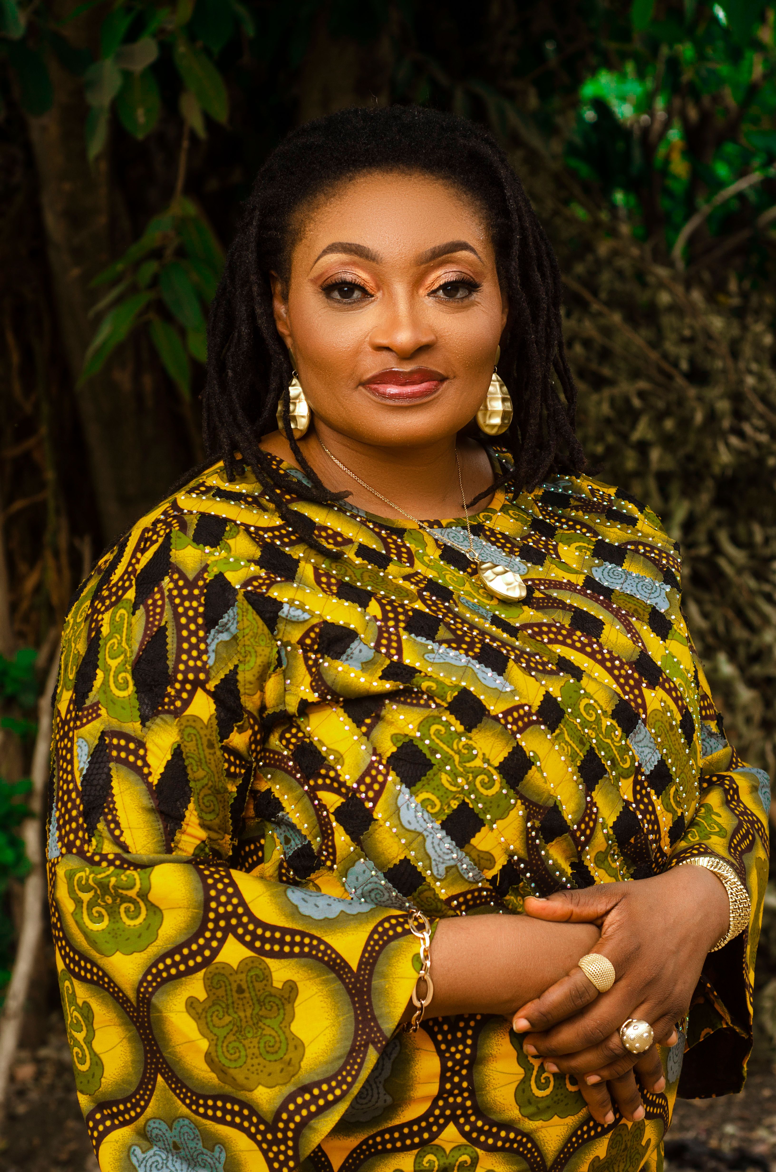 Portrait of a stylish African woman in vibrant traditional attire, displaying jewelry outdoors.