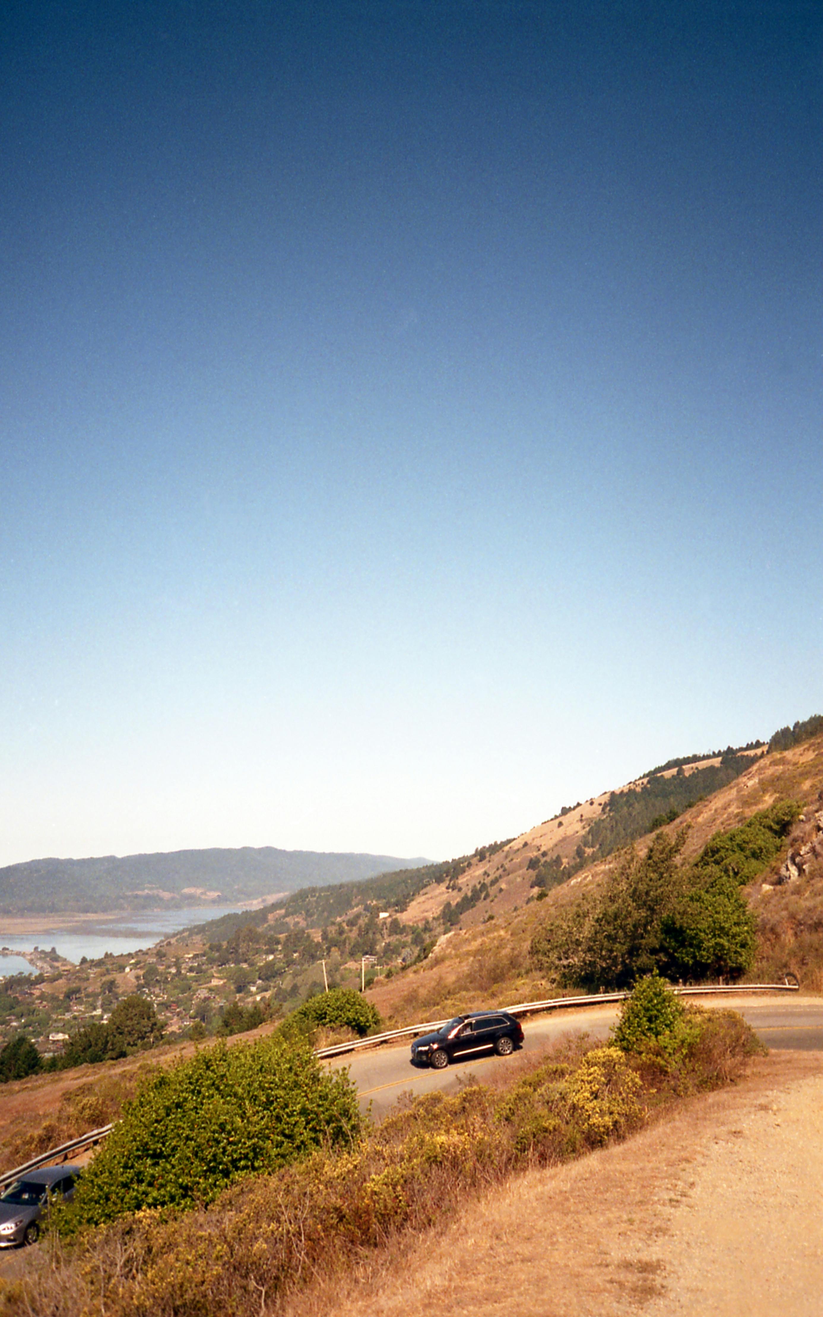 一辆风景秀丽的汽车在晴朗的天空下，沿着蜿蜒的道路穿过加利福尼亚的山丘