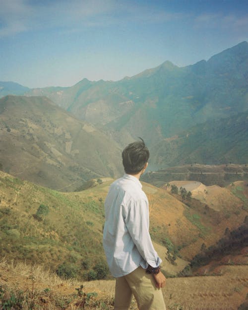 A man standing in the middle of a field looking at the mountains