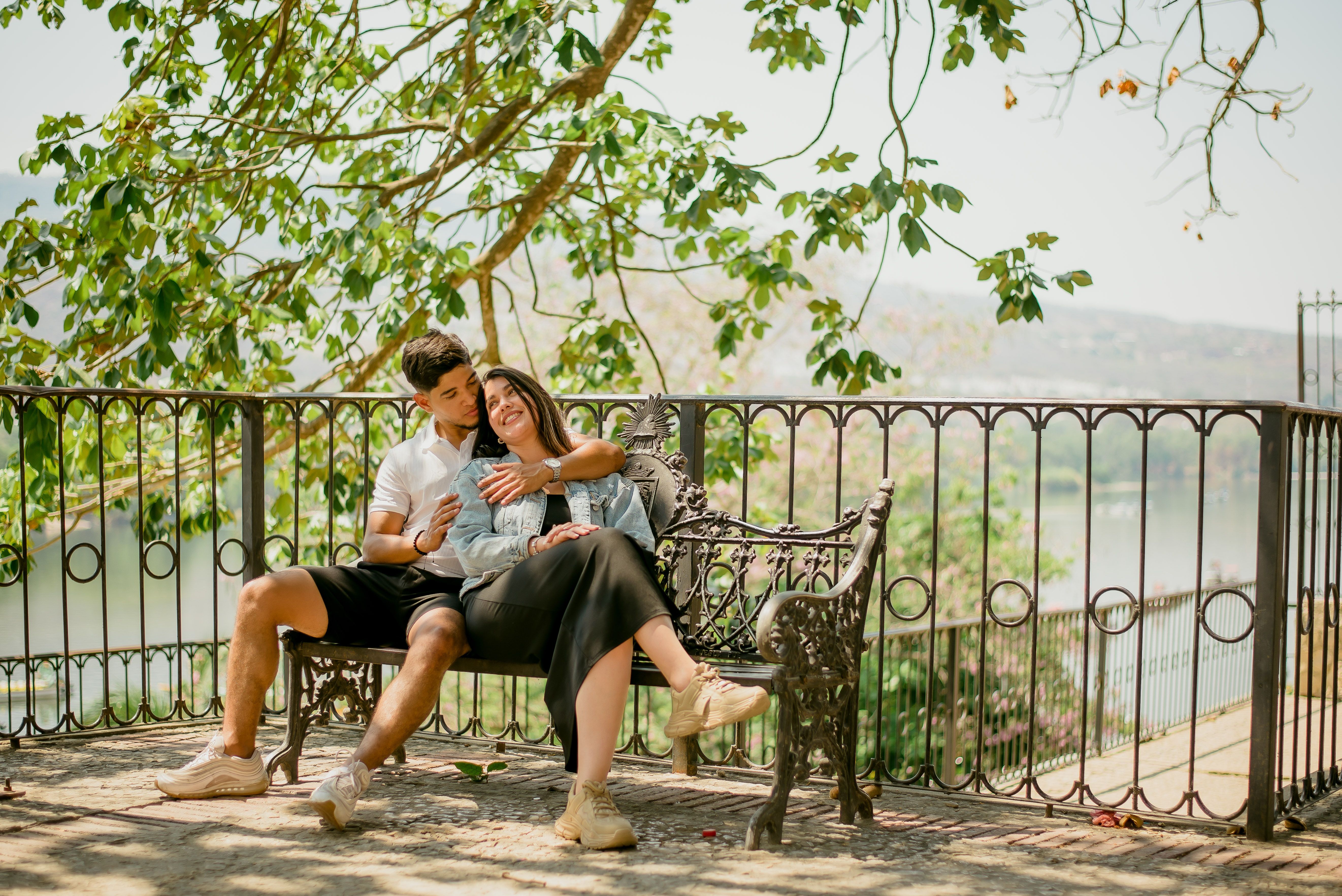 A couple embraces on a park bench under a tree, capturing a serene and romantic moment.