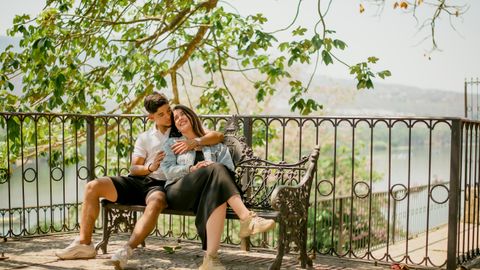 A couple embraces on a park bench under a tree, capturing a serene and romantic moment.